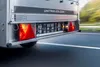 The rear view of a trailer on a road, showing the taillights and license plate holder. Produktbild-Vorschau