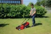 A man is mowing a lawn with a red electric lawnmower in a suburban backyard. Náhled obrázku produktu