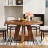 A round wooden dining table with chairs set in a dining room with a fireplace and bookshelf in the background. Podgląd zdjęcia produktu