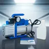 A vacuum pump with a gauge and a bottle of fluid, set against a blurred background. Anteprima dell’immagine prodotto