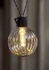 A single decorative light bulb with a ribbed glass design, illuminated from within, hanging from wires. Podgląd zdjęcia produktu