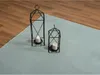 Two black metal lanterns with white candles inside are placed on a light blue rug next to a wooden floor. Produktbild-Vorschau