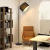 A floor lamp is placed next to a bookshelf and a chair in a room. Produktbild-Vorschau