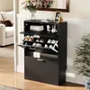 A black shoe cabinet with multiple shelves and drawers, placed in a hallway next to a sofa and a potted plant. The top of the cabinet displays decorative items like a vase of flowers and a framed picture. Náhľad obrázku produktu