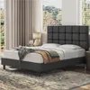A dark gray upholstered bed with a tufted headboard is shown in a bedroom setting with blinds and curtains. Produktbild-Vorschau