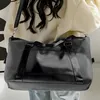 A person wearing a light-colored hoodie and jeans is carrying a black duffel bag over their shoulder. Voir les images du produit