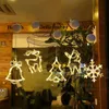 Christmas-themed LED lights hanging in a window, likely a shop or home, with plants and interior visible in the background. Podgląd zdjęcia produktu