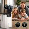 A family is lying on a rug in a living room, with a dehumidifier in the foreground. The dehumidifier has icons for sound, temperature, and a human head with airflow. Náhled obrázku produktu