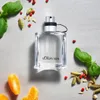 A bottle of s.Oliver Men Eau de Toilette is displayed on a light gray surface, surrounded by various aromatic ingredients like basil leaves, cardamom pods, and red peppercorns, along with slices of tangerine. Produktbild-Vorschau