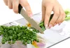 Hands chopping green onions on a cutting board with a floral design. Voir les images du produit