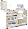 A white sewing table with a sewing machine, spools of thread, and storage bins. Voir les images du produit