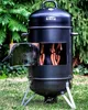 A black smoker barrel with sausages hanging inside, set up in a grassy yard with trees in the background. Podgląd zdjęcia produktu