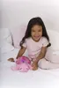 A young girl sitting on a bed with a pink plush turtle toy. Podgląd zdjęcia produktu