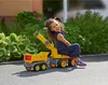 A young girl is happily sitting on a large yellow toy truck with a trailer. Náhled obrázku produktu