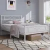 A white metal bed frame with a decorative headboard and footboard is shown in a bedroom setting. Podgląd zdjęcia produktu