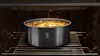 A round baking dish with food inside is placed on a rack inside an oven. Podgląd zdjęcia produktu