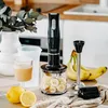 A hand blender and its accessories are displayed on a countertop with fruit and drinks. Produktbild-Vorschau