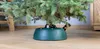 A close-up of a green Christmas tree stand with a Christmas tree trunk in it, placed on a wooden floor. Náhľad obrázku produktu