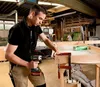 A man is working in a workshop, using a cordless drill to assemble a wooden frame. Produktbild-Vorschau