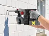 A person wearing gloves is using a cordless hammer drill to drill into a white brick wall. Produktbild-Vorschau