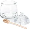 A clear glass honey pot with a lid and a wooden honey dipper, set against a white background. Náhľad obrázku produktu