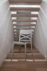 A light gray chair is placed in a hallway with wooden floors and wooden stairs above. Anteprima dell’immagine prodotto