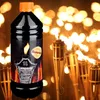 A bottle of lamp oil is in the foreground with several flaming torches in the background. Produktbild-Vorschau