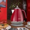 A red electric kettle is placed on a wooden table next to a plate of toast and a cup of tea, with a Japanese-inspired background. Produktbild-Vorschau