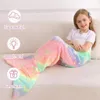 Mädchen sitzt auf einem Sofa, eingewickelt in eine pastellfarbene Regenbogen-Meerjungfrau-Schwanzdecke mit leuchtenden Einhorn- und Sternmustern Produktbild-Vorschau