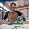 A man wearing safety glasses and gloves is using a Bosch cordless impact wrench to attach a green jig to a wooden surface. Several screws are visible in the foreground. Voir les images du produit