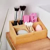 A bamboo organizer filled with makeup brushes, cotton swabs, and makeup sponges on a wooden surface. Náhled obrázku produktu