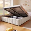 A bed with its storage compartment open, revealing stored items, in a room with a large window. Produktbild-Vorschau