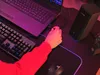 A person's hands are shown plugging a USB cable into a laptop, with a keyboard and speaker on the desk. Produktbild-Vorschau