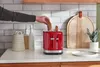A person is placing bread into a red toaster on a kitchen counter. Anteprima dell’immagine prodotto