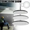 A worker in a yellow hard hat and safety vest is shown in the foreground, with three LED UFO high bay lights hanging in the midground and background. The lights are illuminated. Produktbild-Vorschau