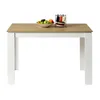 A minimalist dining table with a wooden top and white legs, set against a white background. A bowl of fruit and a plate rack are placed on the table. Náhled obrázku produktu
