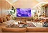 A modern living room with a large TV displaying abstract purple art, surrounded by plants and furniture. Produktbild-Vorschau