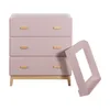 A pink chest of drawers with wooden handles and legs, next to a pink frame. Podgląd zdjęcia produktu