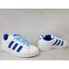 A pair of white Adidas Campus 00s sneakers with blue accents, displayed on a light gray concrete-like surface. Podgląd zdjęcia produktu