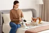 A woman is cleaning a bed with a vacuum cleaner, while a Corgi dog watches. Podgląd zdjęcia produktu