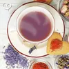 A top-down view of a cup of purple tea, surrounded by dried lavender, saffron, and a heart-shaped cookie topped with saffron. Produktbild-Vorschau