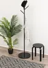 A black stool is placed next to a coat rack with a hat and scarf, with a potted plant and a rug in the foreground. Náhled obrázku produktu