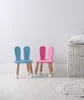 Two children's chairs with bunny ears, a wicker basket with a pillow, and a rug in a room with a white wall and light wooden floor. Produktbild-Vorschau