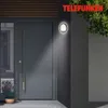 A modern gray front door with a sleek handle and a wall-mounted LED light fixture illuminating the entrance. Produktbild-Vorschau