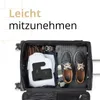 An open suitcase packed with clothing and shoes, with a charging station on top of a white shirt. Produktbild-Vorschau