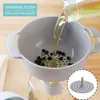 A kitchen funnel with a removable sieve is shown filtering peppercorns from oil into a glass jar. Produktbild-Vorschau