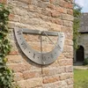 A sundial mounted on a brick wall outdoors, with ivy growing on the wall and a building in the background. Produktbild-Vorschau