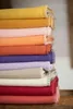 A stack of folded blankets in various pastel and earthy tones. Produktbild-Vorschau