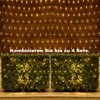 A net light decoration is shown draped over a wooden wall, with two bushes in the foreground also decorated with lights. Náhľad obrázku produktu