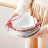 A person holding a stack of white and red patterned plates and bowls. Náhled obrázku produktu